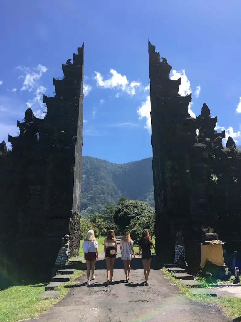 Students walking through a traditional Balinese split gate with mountains and tropical greenery in Bali.