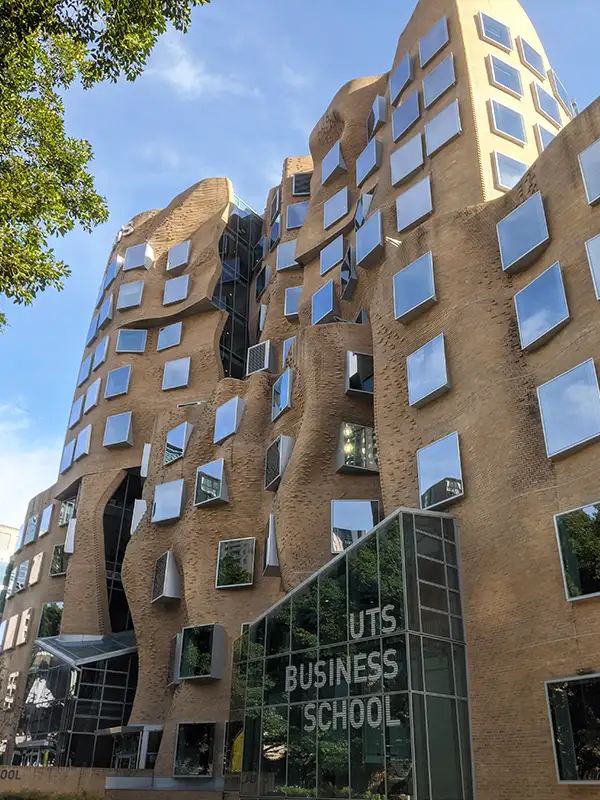 Sculptural brown brick facade of the UTS Business School building with irregular mirrored windows and a glass entrance in Sydney