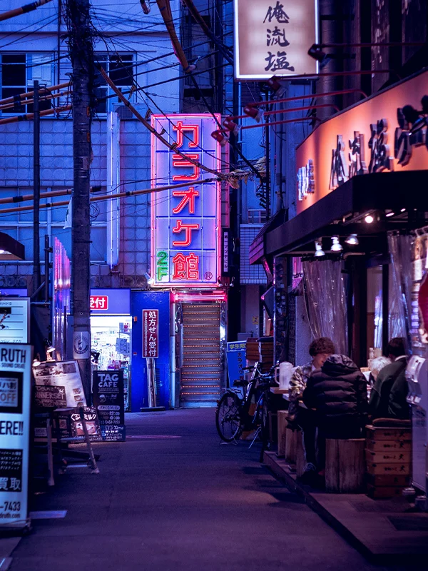 Neon-lit street in Tokyo with restaurants and students enjoying urban nightlife in Japan.