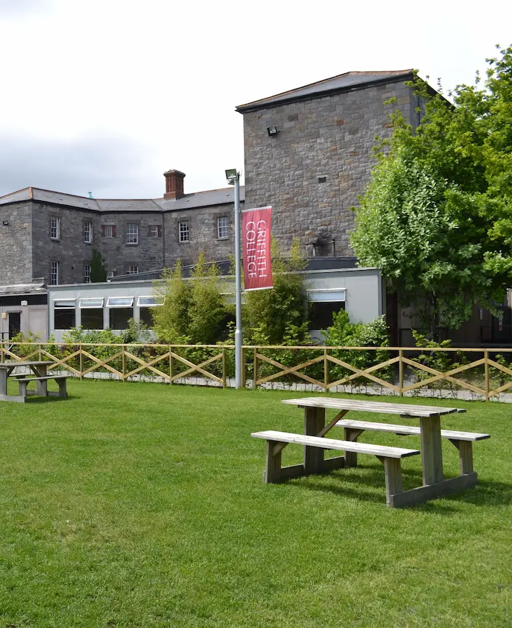 Historic stone building and green lawn with picnic tables at Griffith College Dublin campus in Ireland.