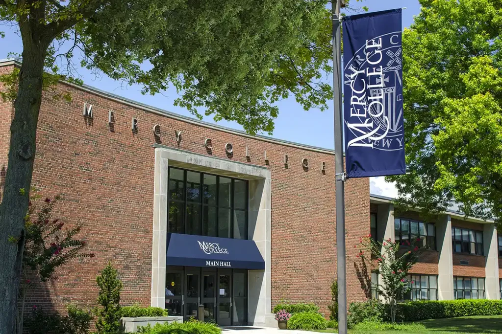 Main Hall building at Mercy University campus in New York with trees and lawn.