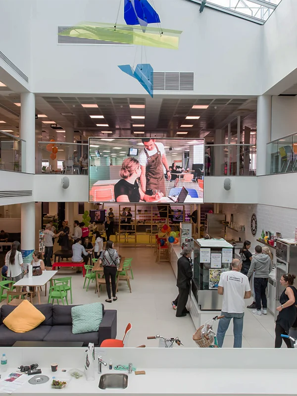 Busy Torrens University open plan atrium with colourful chairs, a large LED screen and hanging art installations above students socialising on multiple floors